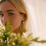 Woman wearing a veil and diamond sun earrings with a floral bouquet in the foreground