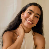 Woman wearing sun-shaped diamond earrings and a blue sapphire ring, smiling against a neutral background