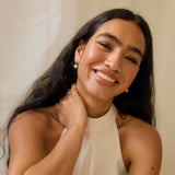 Woman wearing earrings and a necklace, smiling against a neutral background
