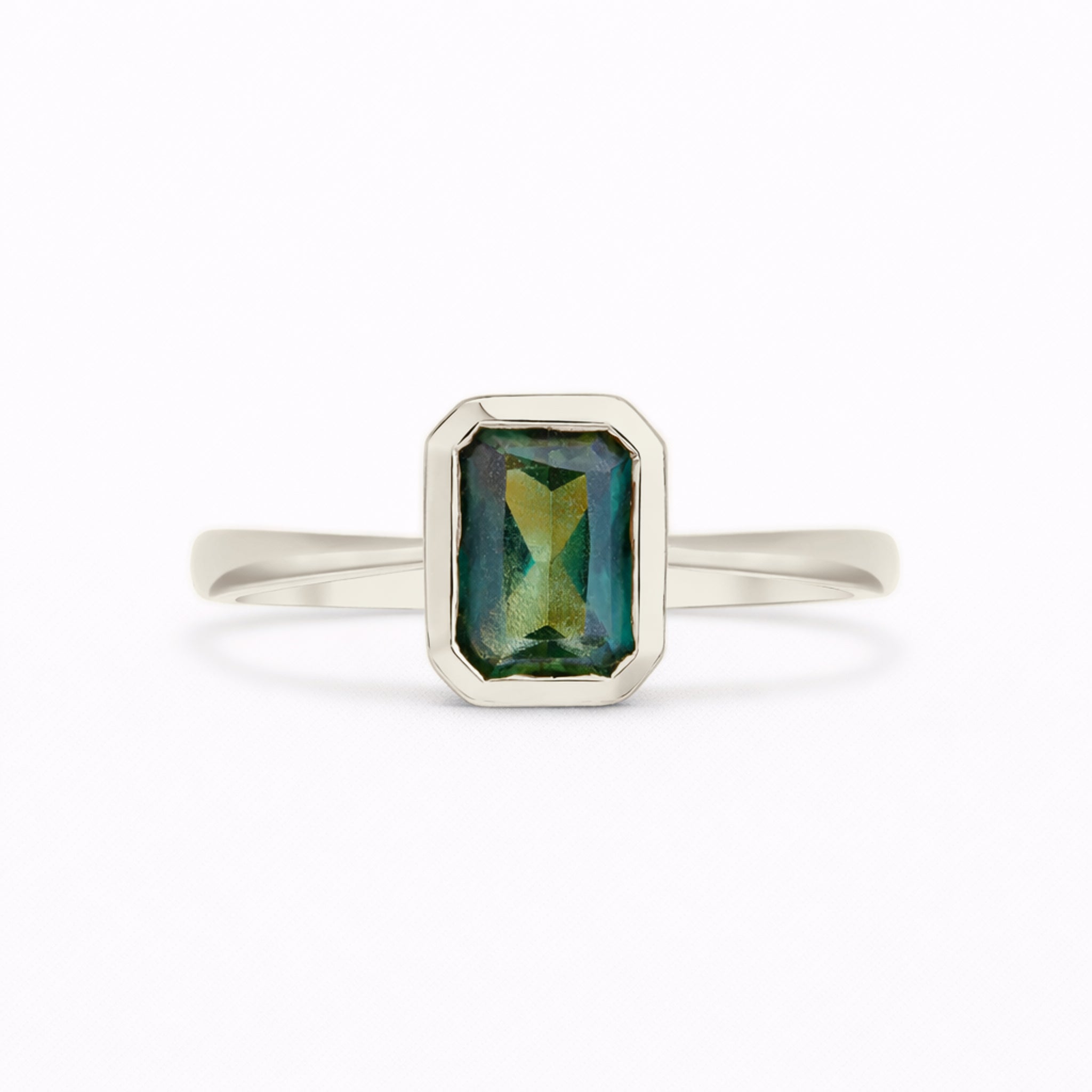 A white gold ring with a rectangular emerald-cut green gemstone featuring iridescent blue and gold reflections, set against a plain white background.