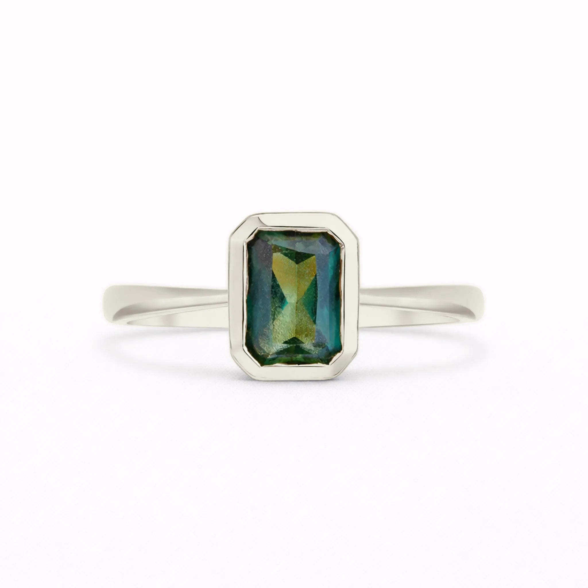 A white gold ring with a rectangular emerald-cut green gemstone featuring iridescent blue and gold reflections, set against a plain white background.