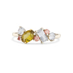 A yellow-green marquise-cut gemstone ring set in a white gold band, flanked by clear round and baguette-cut stones and small pink round stones, on a white background.
