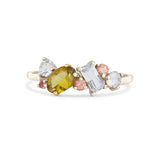 A yellow-green marquise-cut gemstone ring set in a white gold band, flanked by clear round and baguette-cut stones and small pink round stones, on a white background.