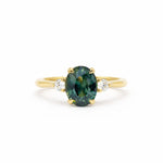 Gold ring with a greeny teal blue gemstone and smaller diamonds on a white background