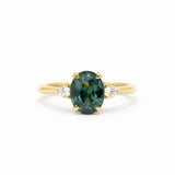 Gold ring with a greeny teal blue gemstone and smaller diamonds on a white background