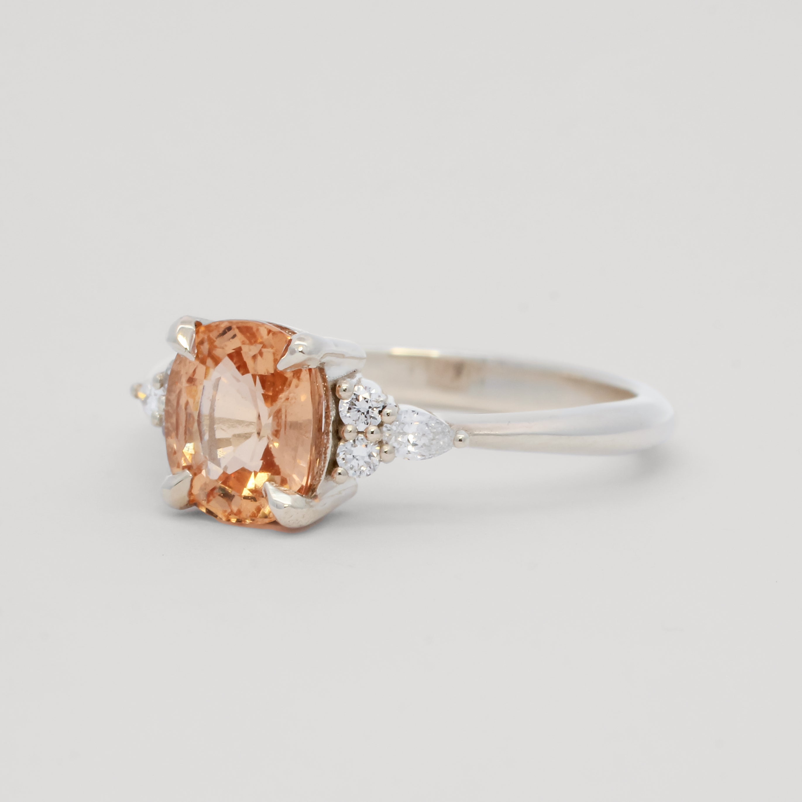 side view of a white gold ring with a large orange gemstone on a light gray background