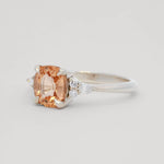side view of a white gold ring with a large orange gemstone on a light gray background