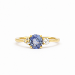 engagement ring with round cornflower blue sapphire, with asymmetric accent diamonds on a white background