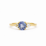engagement ring with round cornflower blue sapphire, with asymmetric accent diamonds on a white background