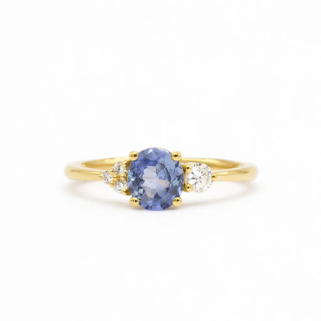 engagement ring with round cornflower blue sapphire, with asymmetric accent diamonds on a white background