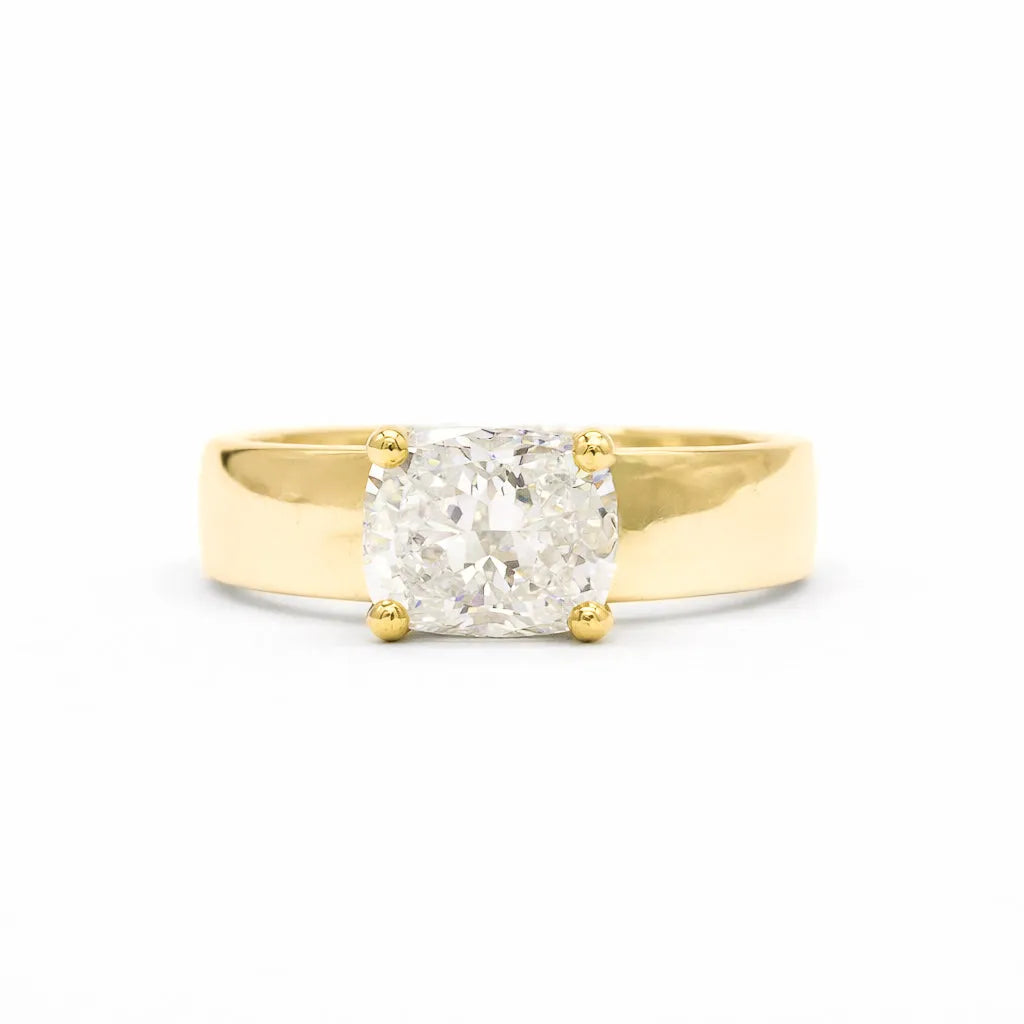 A chunky yellow gold engagement ring with a cushion-cut diamond set in a four-prong setting, photographed against a seamless white background.