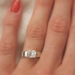wide band white gold engagement ring with cushion cut diamond on a hand with red nail varnish