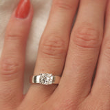wide band white gold engagement ring with cushion cut diamond on a hand with red nail varnish