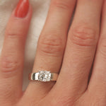 wide band white gold engagement ring with cushion cut diamond on a hand with red nail varnish