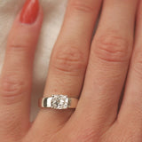 wide band white gold engagement ring with cushion cut diamond on a hand with red nail varnish