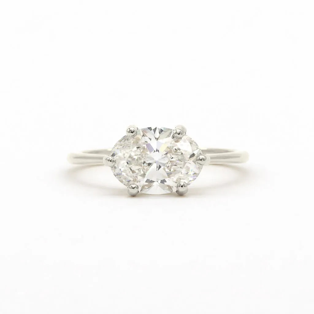 A classic solitaire engagement ring featuring an oval brilliant-cut diamond set east-to-west with four-prongs in a white gold or platinum band, centered on a seamless white background
