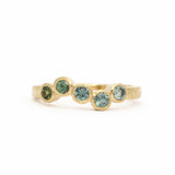 gold waved engagement ring with five round bezel set sapphires in an ombre from green to light blue on a white background