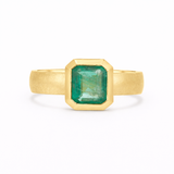chunky wide band gold engagement ring with bezel set green emerald gemstone on a white background