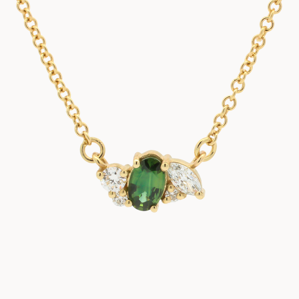 A gold chain necklace featuring a wing-shaped pendant with a central green oval sapphire with marquise and round accent diamonds, shown on a plain light background.
