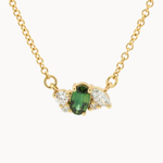 A gold chain necklace featuring a wing-shaped pendant with a central green oval sapphire with marquise and round accent diamonds, shown on a plain light background.
