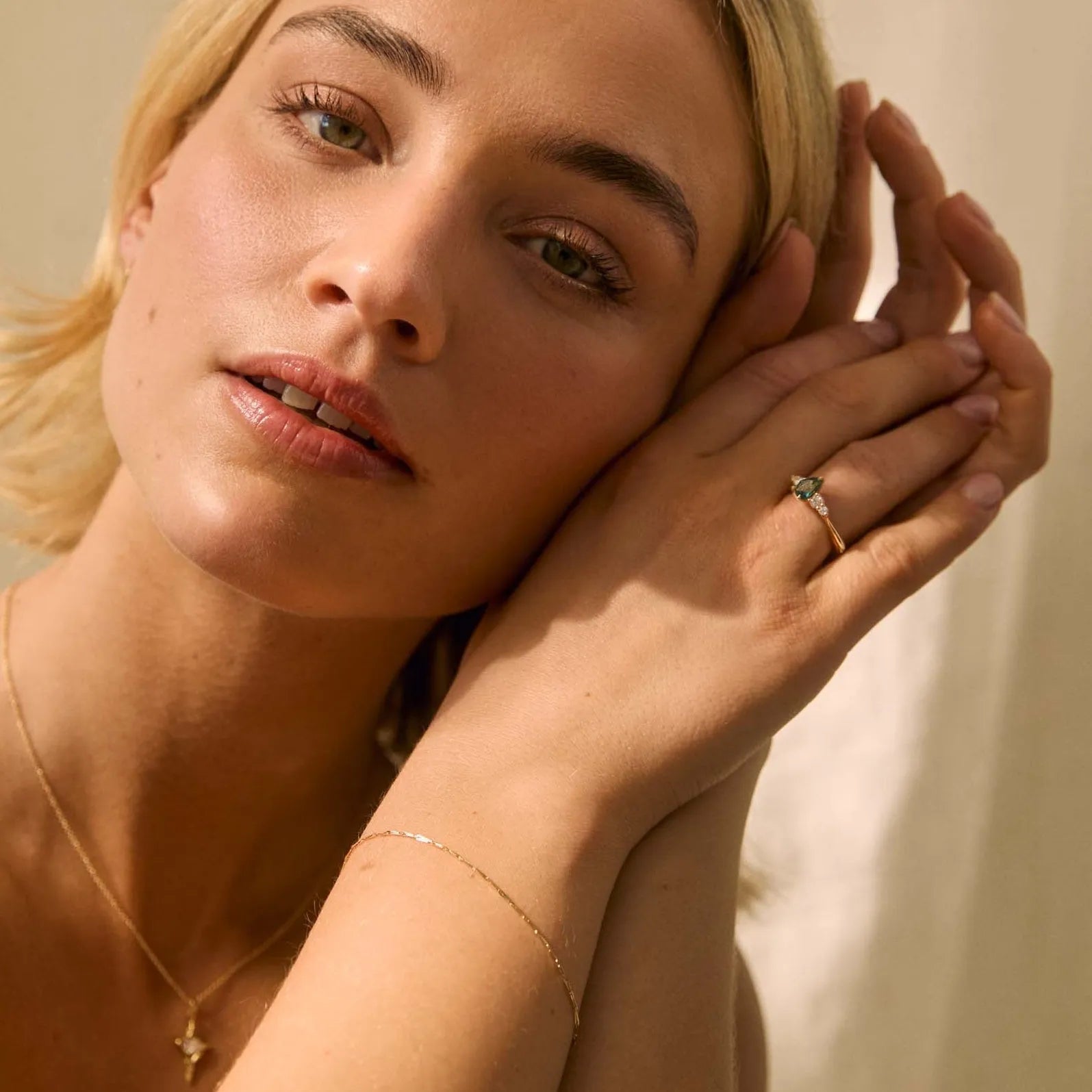 woman wearing pear sapphire engagement ring with tapered diamonds, a gold bracelet and necklace