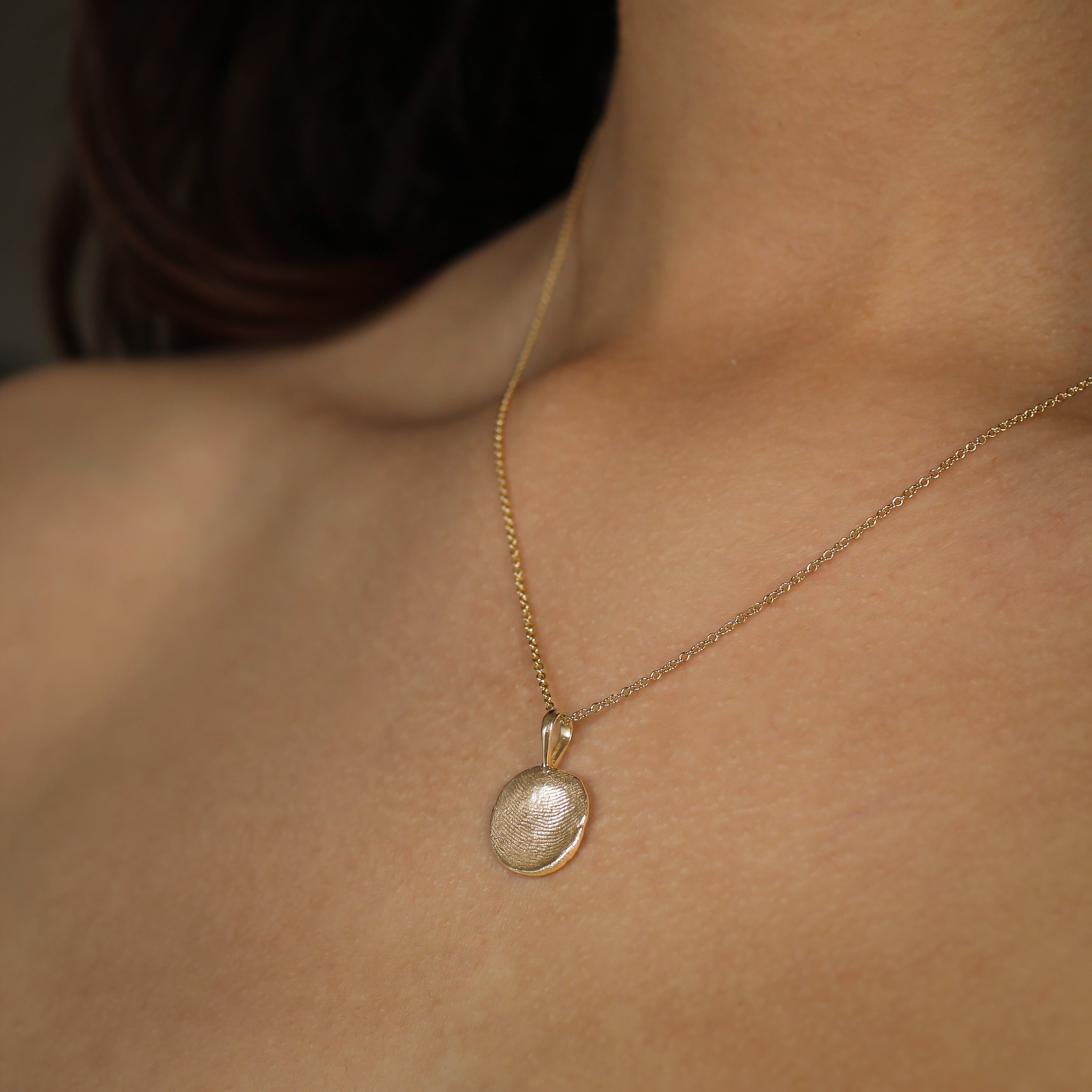 Gold necklace with a fingerprint pendant on a person's neck