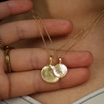 Two gold necklaces with round pendants with fingerprint texture on a person's hand.