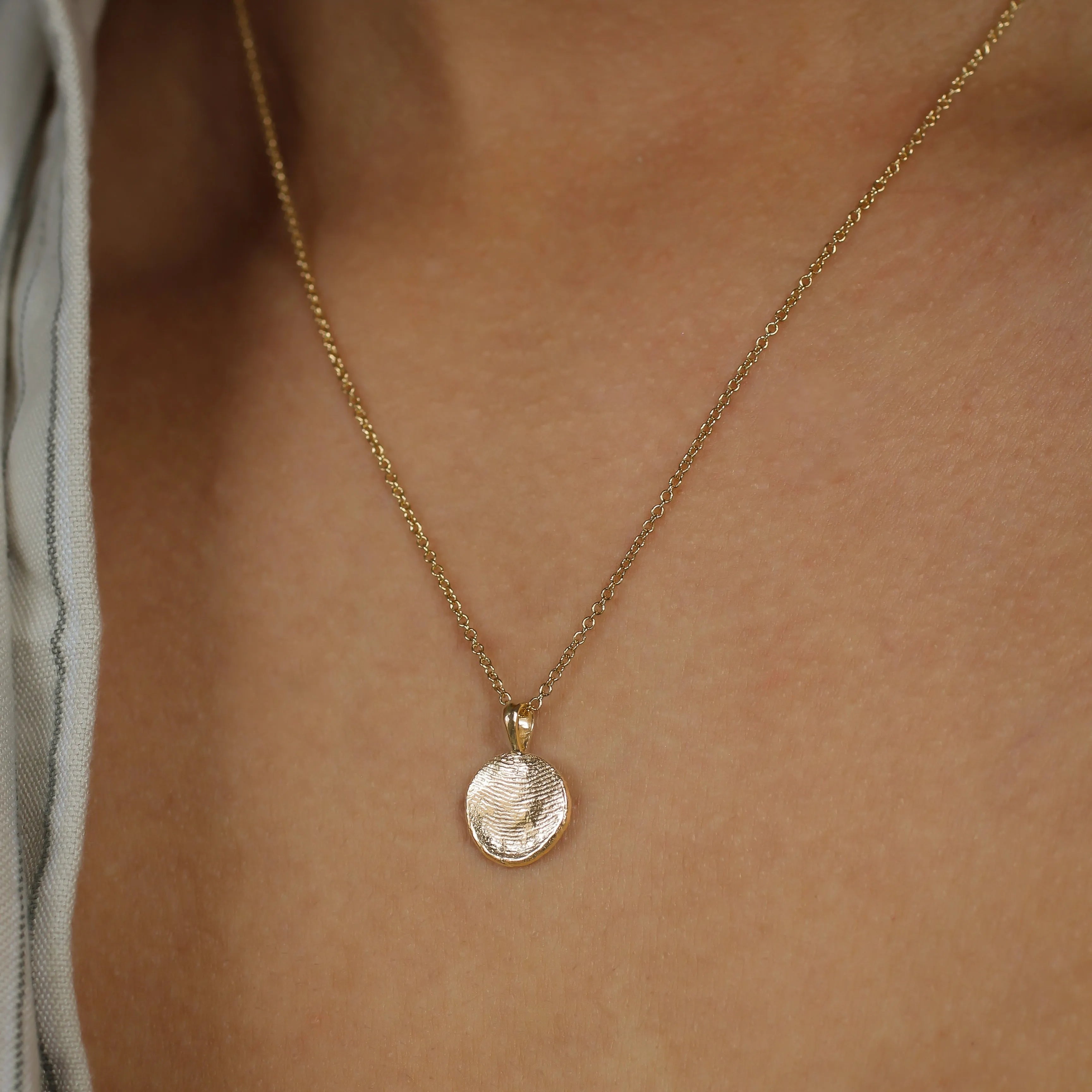 Gold necklace with a small fingerprint pendant on a person's neck