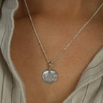 Silver necklace with a large fingerprint textured pendant on a person wearing a striped shirt.
