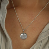 Silver necklace with a large fingerprint textured pendant on a person wearing a striped shirt.
