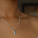 Close-up of a silver necklace with a pendant on a person's neck.