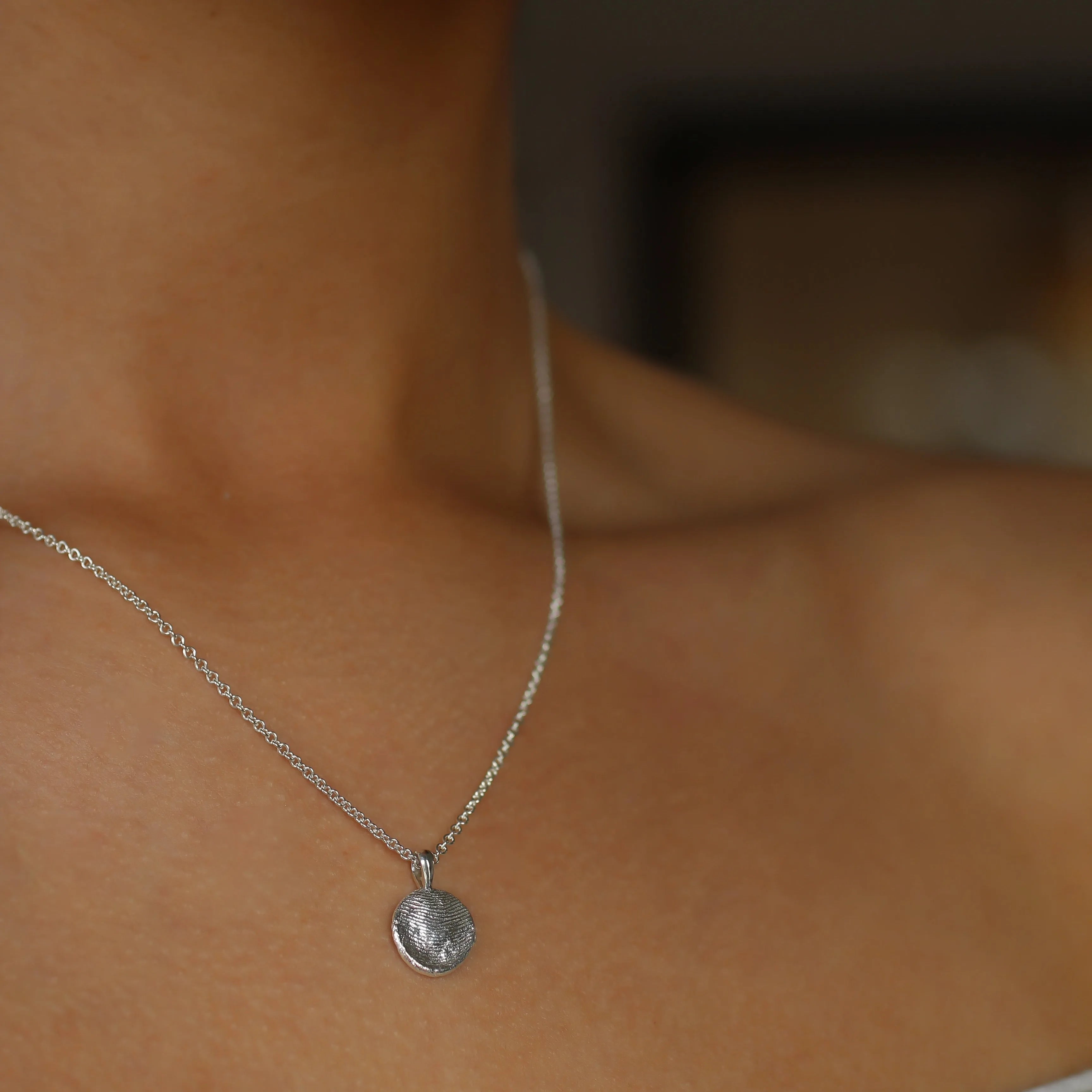 Close-up of a silver necklace with a pendant on a person's neck.
