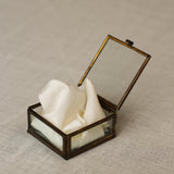 Decorative box with a glass lid containing white ribbon on a textured surface