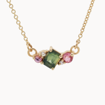 Gold necklace with a green gemstone and pink stones on a white background