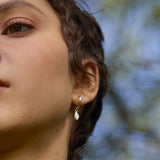 Close-up of a person wearing a gold oak leaf earring with a blurred natural background of trees