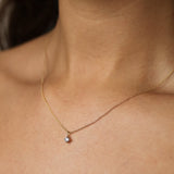 Gold necklace with a small diamond pendant on a person's neck against a neutral background