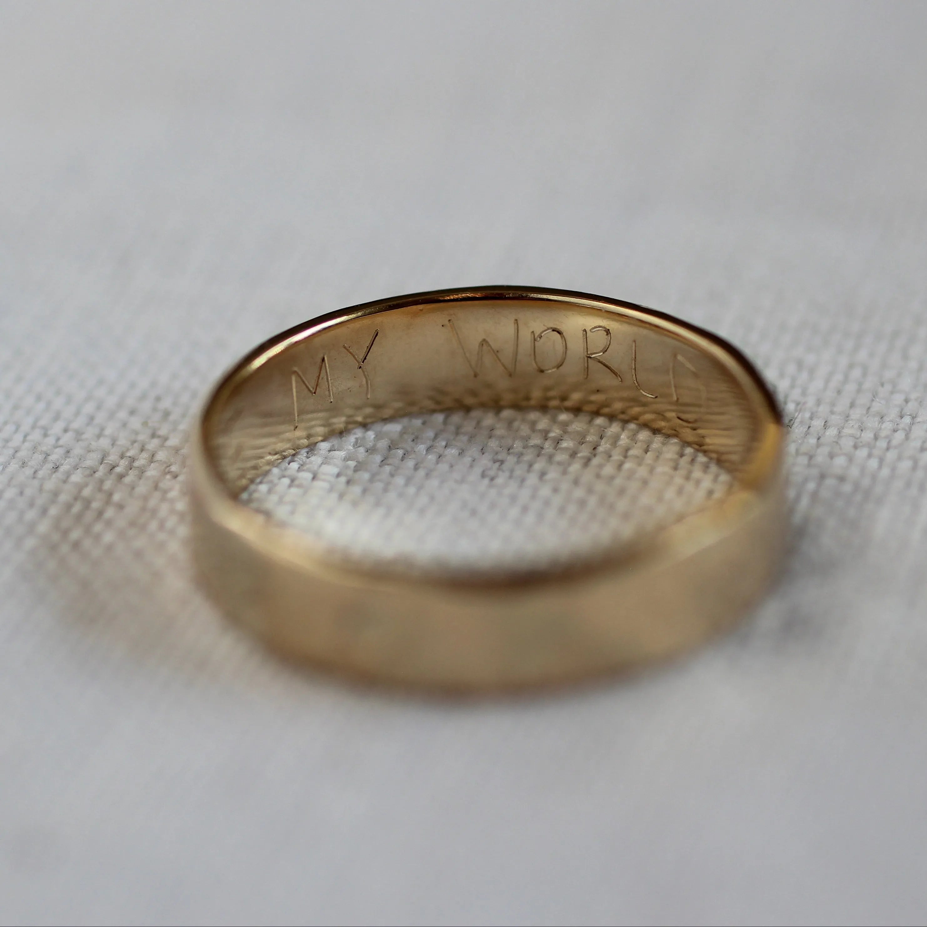 Engraved gold ring with handwritten words 'my world' in capital letters on the inside of the ring