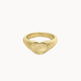 A textured gold signet ring with a heart-shaped face, photographed on a clean, solid off-white background.
