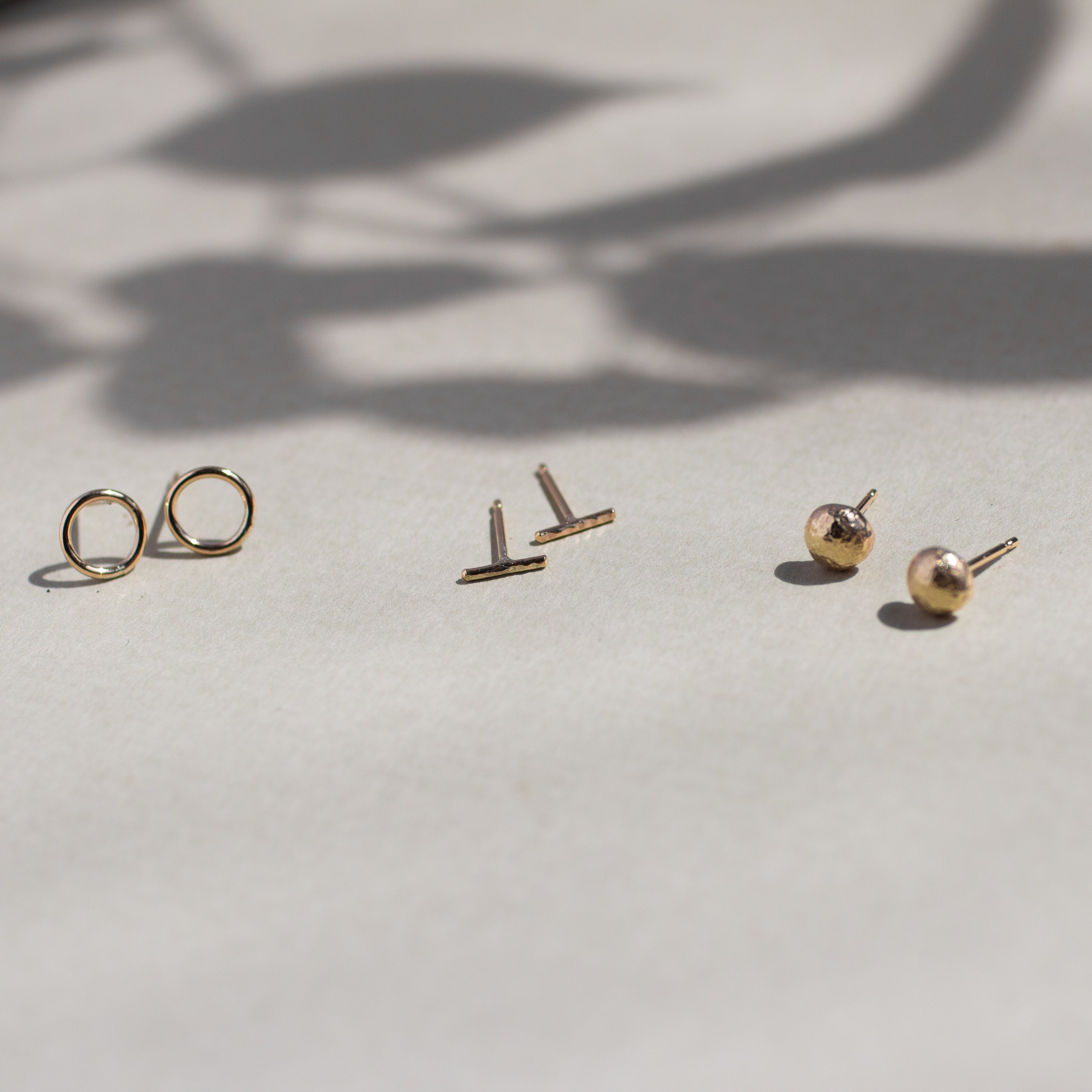 Circle, bar and pebble studs in gold with leaf shadow