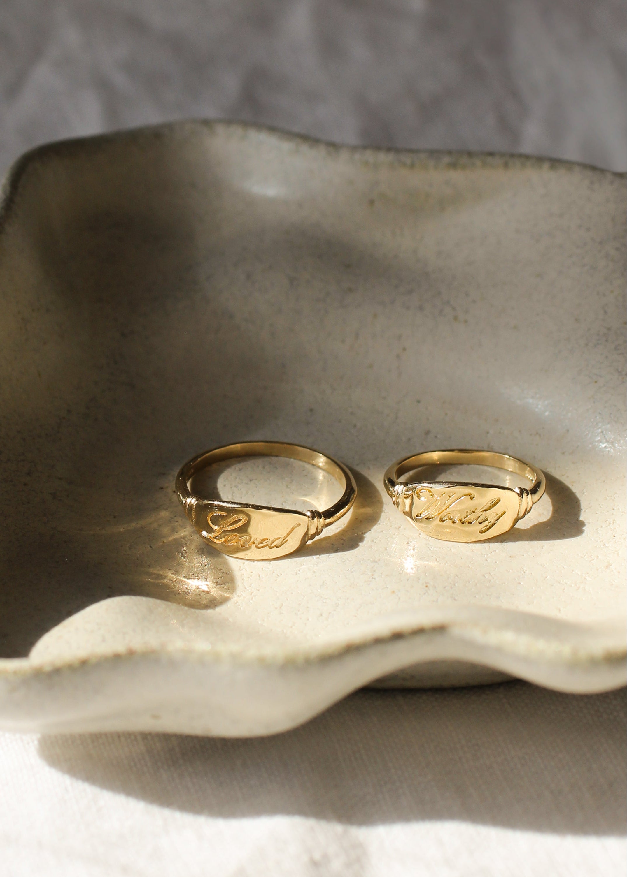 Two gold rings on a textured ceramic dish with a neutral background