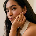 model with hand to her face wearing a blue/green sapphire asymmetric diamond cluster engagement ring
