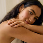 woman smiling to camera resting her arms on her shoulder wearing lowfit green sapphire trilogy engagement ring