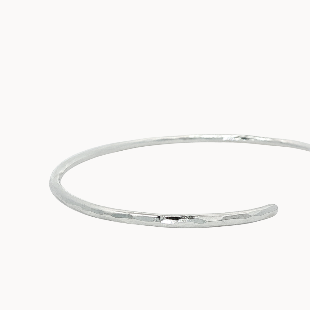 close up of hammered texture on open silver bangle on a white background