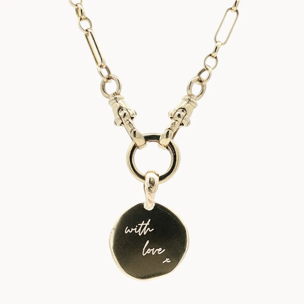 close up of a gold chunky chain necklace with round organic pendant engraved with handwritten 'with love x' on a white background