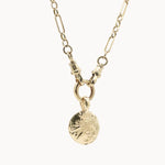 Gold statement necklace with a round textured pendant on a white background