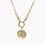 Gold necklace with a round textured pendant on a white background