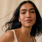 Woman wearing a diamond drop earrings and v neck wedding dress against a beige background