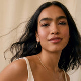 Woman wearing a diamond drop earrings and v neck wedding dress against a beige background