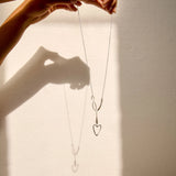 Person holding a necklace with heart pendants against a neutral background