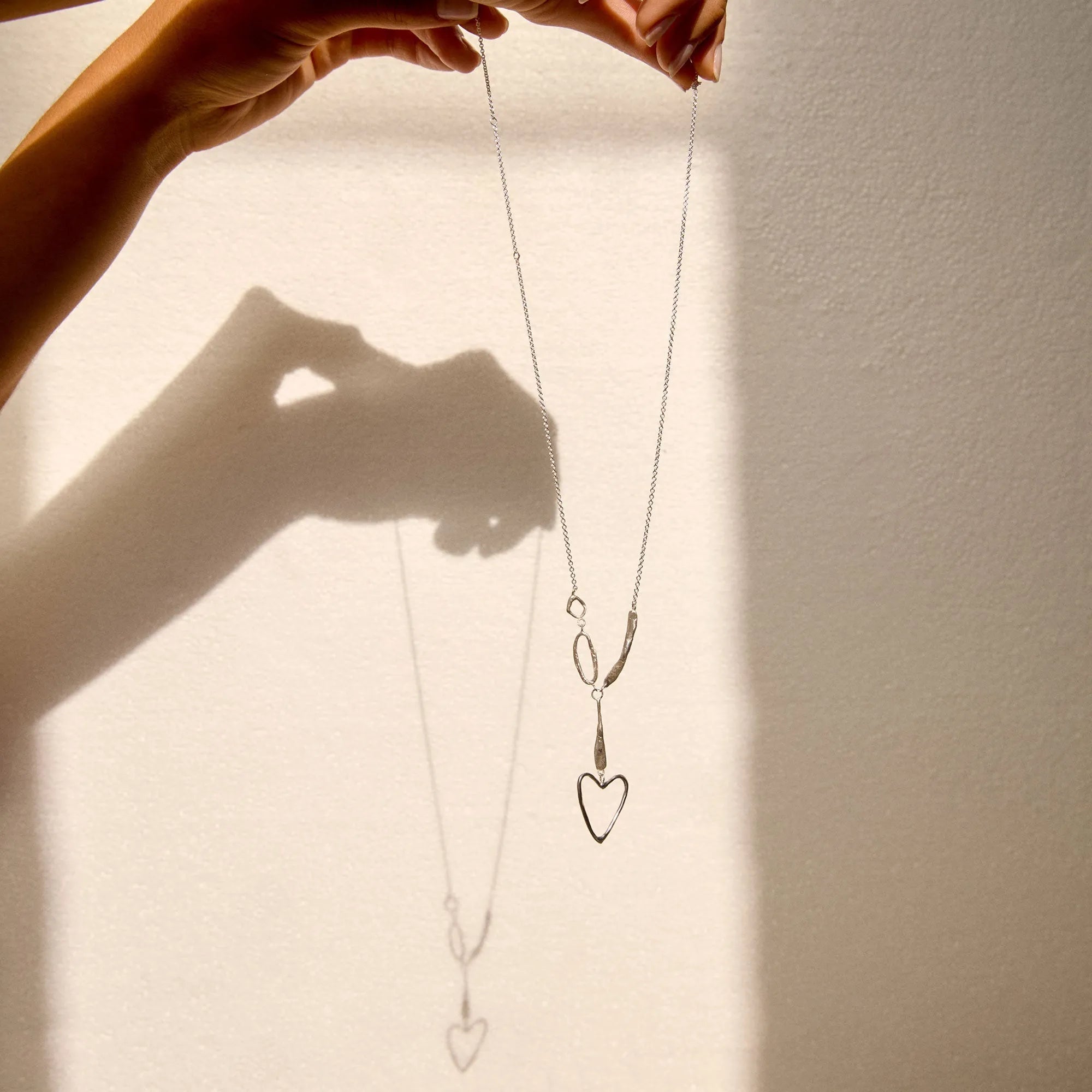 Person holding a necklace with heart pendants against a neutral background